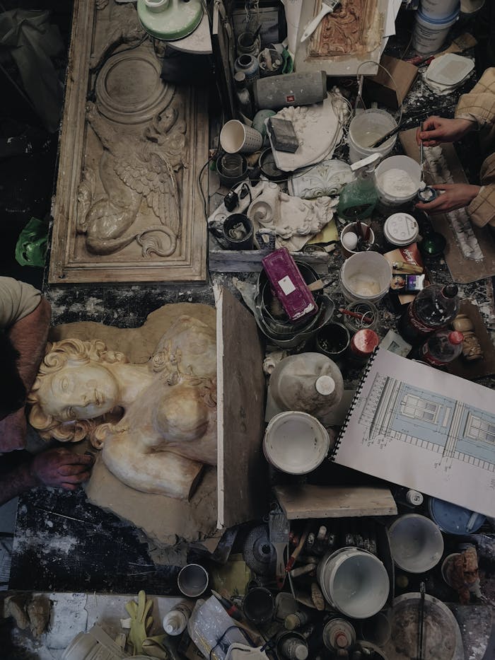 Explore a cluttered artisan workshop filled with sculpting tools, drawings, and intricate sculptures in progress.